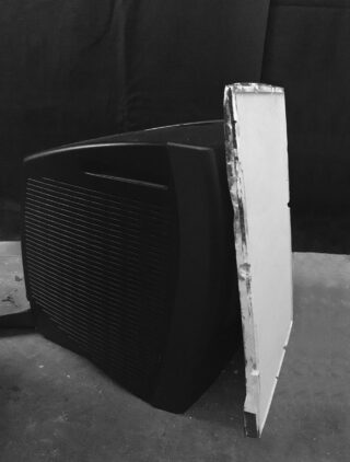 Ein schwarzer Kathodenstrahlröhrenmonitor (CRT) liegt auf der Seite, die Frontplatte ist entfernt, sodass der innere Bildschirm vor einem dunklen Hintergrund sichtbar ist.