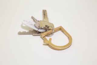 Ein Schlüsselbund mit einem goldfarbenen Schlüsselanhänger aus Metall, fotografiert auf einem schlichten weißen Hintergrund.