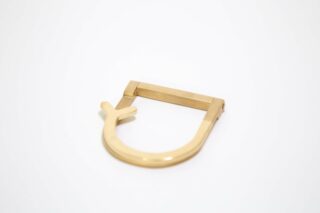 Ein goldfarbenes Metallobjekt mit einem flachen Stab und einer abgerundeten, offenen Schlaufe mit einer kleinen hervorstehenden Lasche auf einer Seite, platziert auf einem schlichten weißen Hintergrund.