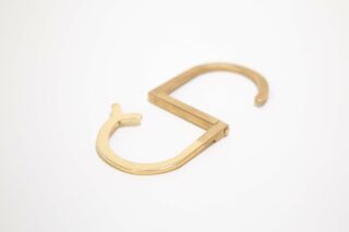 Haken-Accessoire aus goldenem Metall, dessen eines Ende die Form eines Fragezeichens hat und dessen anderes Ende gerade ist, auf weißem Hintergrund platziert.