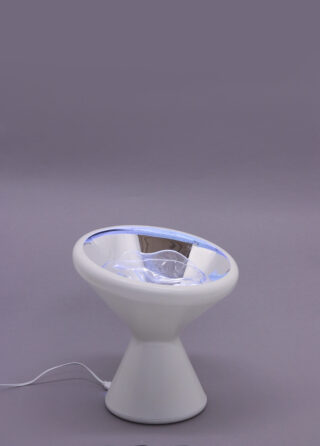 Eine moderne, weiße, kegelförmige Tischlampe mit reflektierender Innenfläche und Netzkabel vor einem schlichten grauen Hintergrund.