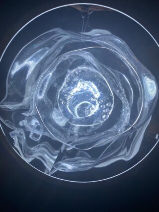 Eine Nahaufnahme des Inneren eines transparenten Plastikbechers mit Wasser- und Luftblasen, von oben beleuchtet, mit sichtbaren Lichtreflexionen und Verzerrungen.