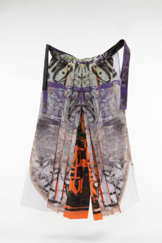 Ein Faltenrock mit abstrakten, mehrfarbigen Drucken in Grau-, Orange-, Schwarz- und Lilatönen vor einem schlichten weißen Hintergrund.