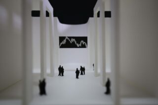 Miniaturfiguren stehen zwischen hohen weißen Säulen in einer modernen, minimalistischen Halle mit einem schwarz-weißen geometrischen Kunstwerk an der gegenüberliegenden Wand.