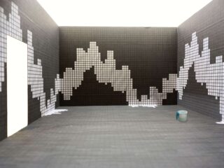 Ein gefliester Raum mit schwarz-weißen Pixelmustern an den Wänden, einem hellen Türrahmen auf der linken Seite und einem blau-grauen Becher auf dem Boden auf der rechten Seite.