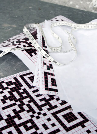 Auf einer grauen Fläche sind ein Maßband, Millimeterpapier und Blätter mit schwarz-weißen geometrischen Mustern ausgebreitet.