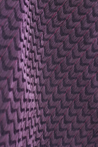 Nahaufnahme eines violett-schwarzen strukturierten Stoffes mit einem sich wiederholenden Zickzack- und Rautenmuster.