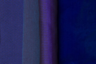 Vier Stoffrollen in Blau- und Lilatönen mit unterschiedlichen Texturen und Mustern werden nebeneinander ausgestellt.