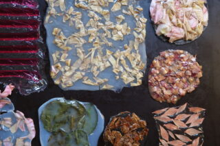 Auf einer dunklen Oberfläche sind verschiedene durchscheinende Blätter angeordnet, in die getrocknete organische Materialien wie Blütenblätter und Blätter eingebettet sind.