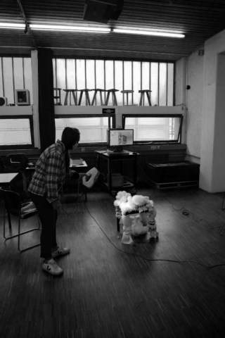 Eine Person bedient ein an einen Computer angeschlossenes Handgerät, während sie in einem Raum mit großen Fenstern und Hockern auf der Fensterbank ein schafförmiges Objekt scannt.