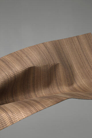 Ein Blatt aus hellbraunem Material mit einem schwarzen Gittermuster ist vor einem schlichten grauen Hintergrund in eine glatte, wellenförmige Form gebogen.