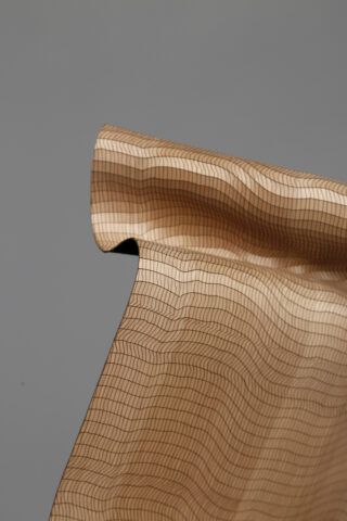 Ein dünner, hellbrauner Stoff mit gitterartigem Muster ist teilweise gewellt vor einem schlichten grauen Hintergrund.