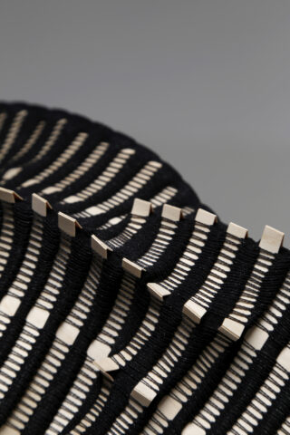 Nahaufnahme eines gemusterten Objekts mit abwechselnd schwarz und beige gewebten oder verflochtenen Materialien, wodurch ein geometrisches, strukturiertes Design entsteht.