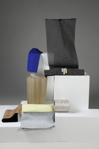 Verschiedene strukturierte und gemusterte Stoffmuster in unterschiedlichen Farben und Formen werden auf weißen Blöcken vor einem grauen Hintergrund angezeigt.