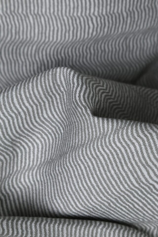 Nahaufnahme eines grau-weißen Stoffes mit kleinen wellenförmigen Streifenmustern, die Falten und Struktur zeigen.