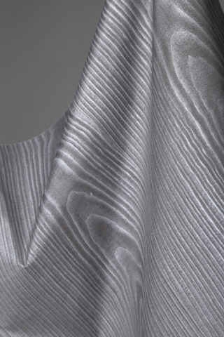 Nahaufnahme eines drapierten Stoffes mit einem welligen, holzmaserungsähnlichen Muster in Grau- und Weißtönen.