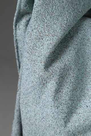 Nahaufnahme eines hellblauen strukturierten Stoffes mit kleinen Sprenkeln, die eine Falte oder Knickstelle im Material zeigen.