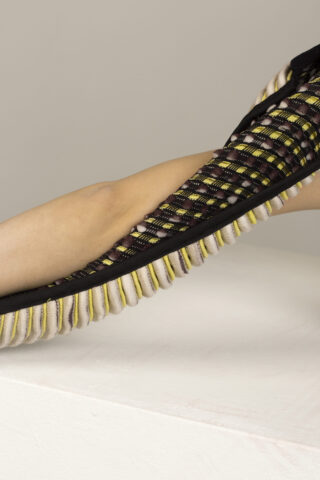 Der Arm einer Person ruht auf einer weißen Oberfläche, die teilweise von einem schwarzen, gewebten, netzartigen Ärmel mit gelben und weißen Akzenten bedeckt ist.