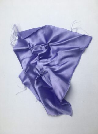 Auf einem schlichten weißen Hintergrund liegt ein Stück glänzender lavendelfarbener Stoff mit unregelmäßigen Rändern, der an mehreren Stellen gerafft und verknotet ist.