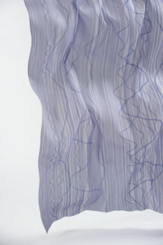 Ein halbtransparenter, weißer Stoff mit dünnen, wellenförmigen blauen Linien, die locker vor einem schlichten hellen Hintergrund hängen.