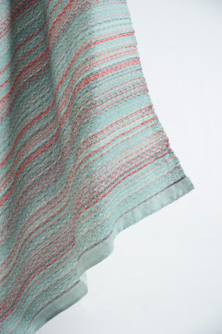 Eine Nahaufnahme eines strukturierten Stoffes mit horizontalen roten und silbernen Streifen auf hellblauem Hintergrund, drapiert vor einer weißen Oberfläche.