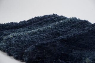 Eine Nahaufnahme eines dunkelblauen, zotteligen Teppichs oder Läufers auf einem schlichten weißen Hintergrund.