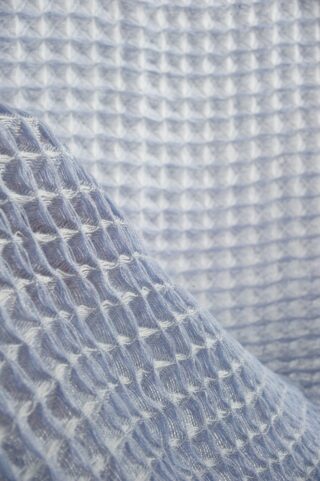 Nahaufnahme eines hellblauen Stoffes mit Waffelstruktur, der sein gitterartiges Muster und seine dreidimensionale Oberfläche zeigt.