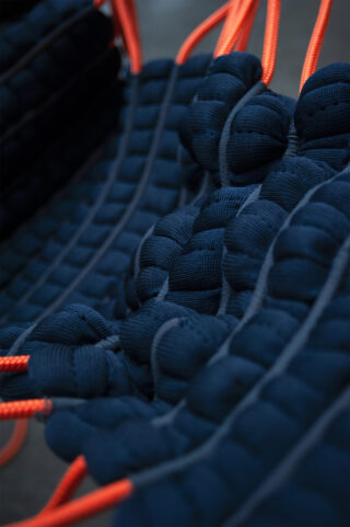 Nahaufnahme eines dunkelblauen Gewebes mit durchgezogenen orangefarbenen Kordeln, die Reihen strukturierter, gepolsterter Abschnitte bilden.