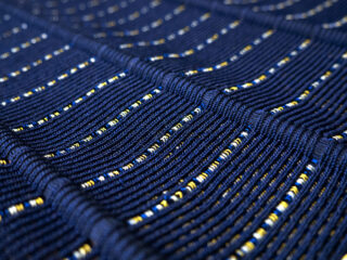 Nahaufnahme eines strukturierten blauen Stoffes mit horizontalen Reihen aus gelben und weißen Akzenten, die ein gitterartiges Muster bilden.