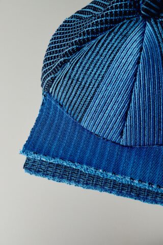 Nahaufnahme einer blau-schwarzen Strickmütze mit Struktur vor einem schlichten hellen Hintergrund.
