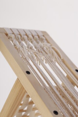 Nahaufnahme eines Holzrahmens mit gewebten weißen Kordeln, der einen Teil eines Stuhls oder Hockers vor einem schlichten Hintergrund zeigt.