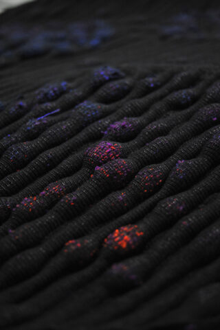 Nahaufnahme eines strukturierten schwarzen Stoffes mit erhabenen, abgerundeten Beulen mit kleinen roten, violetten und blauen Flecken.