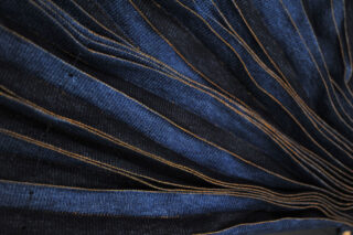 Nahaufnahme eines dunkelblauen Stoffes mit orangefarbenen Nähten, die ein plissiertes, fächerartiges Muster bilden.