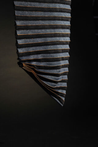 Vor einem schwarzen Hintergrund ist ein gefaltetes Stück dunkler Jeansstoff mit orangefarbenen Nähten zu sehen.