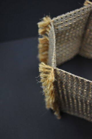 Eine Nahaufnahme eines geflochtenen, rechteckigen Korbs mit ausgefransten Rändern, der auf einer dunklen Oberfläche steht.