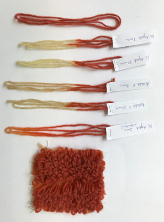 Sechs beschriftete Garnproben mit Ombre-Farbtönen von Creme bis Orange sind über einem kleinen Muster aus strukturiertem, orangefarbenem Garn angeordnet.