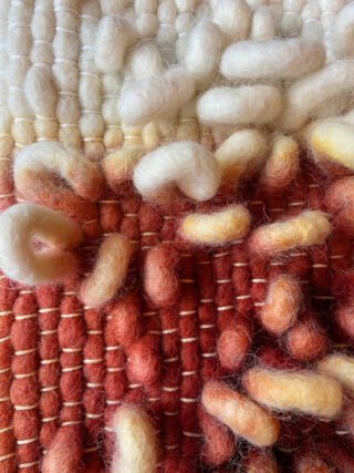 Nahaufnahme eines strukturierten gewebten Textils mit dicken Wollfasern in Creme-, Gelb- und Rotbrauntönen mit erhabenen, geschlungenen Elementen.