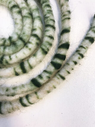 Drei Spulen aus flauschigem, grün-weiß gestreiftem Seil sind auf einer flachen weißen Oberfläche angeordnet.