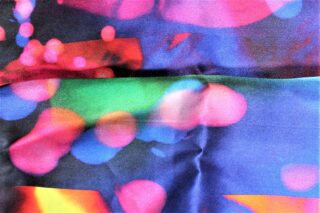 Eine Nahaufnahme eines Stoffes mit einem farbenfrohen abstrakten Muster, das verschwommene Kreise und Formen in Rosa, Blau, Grün, Orange und Lila aufweist.