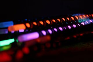 Reihen von Leuchtstäben in verschiedenen Farben, darunter Orange, Lila, Grün und Rot, leuchten vor einem dunklen Hintergrund.