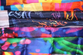 Sechs Streifen aus buntem, gemustertem Stoff sind horizontal ausgelegt und zeigen verschiedene abstrakte und geometrische Designs in lebendigen Farbtönen.
