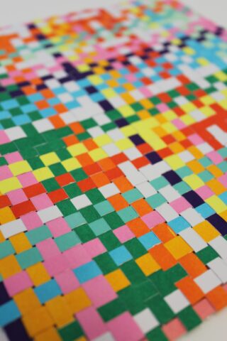 Nahaufnahme eines farbenfrohen Mosaiks aus kleinen quadratischen Kacheln, die in einem Gittermuster angeordnet sind und eine Vielzahl leuchtender Farben aufweisen, darunter Grün, Orange, Gelb, Blau, Rosa und Rot.