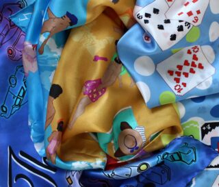 Bunte, gemusterte Seidenschals mit Abbildungen von schwimmenden Menschen, Spielkarten, Autos und abstrakten Formen sind in einer Nahaufnahme übereinandergeschichtet und überlappen sich.
