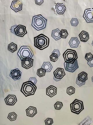 Schwarze sechseckige konzentrische Formen in verschiedenen Größen sind auf einer halbtransparenten, zerknitterten weißen Oberfläche angeordnet, darunter sind einige Papiere schwach sichtbar.