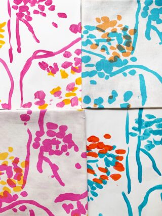 Vier quadratische Leinwände, die in einem Raster angeordnet sind, jede mit abstrakten Blumenmustern in rosa, gelber, blauer und orangefarbener Farbe auf weißem Hintergrund.