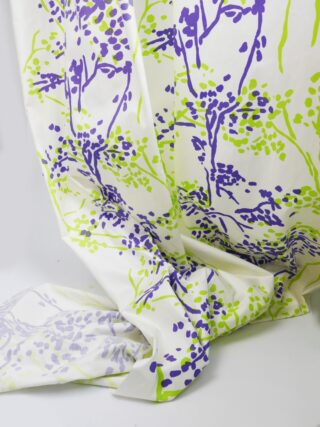 Ein drapierter weißer Stoff mit einem abstrakten Blumenmuster in Lila und Grün auf schlichtem Hintergrund.