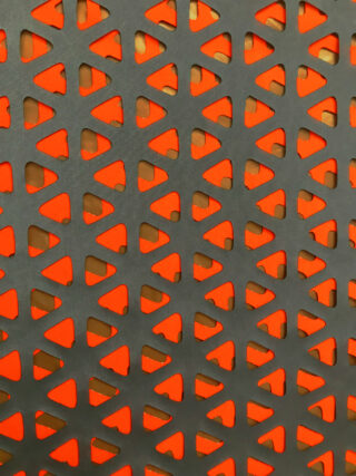 Nahaufnahme einer schwarzen perforierten Oberfläche mit sich wiederholenden dreieckigen Ausschnitten, die einen orangefarbenen Hintergrund freigeben.