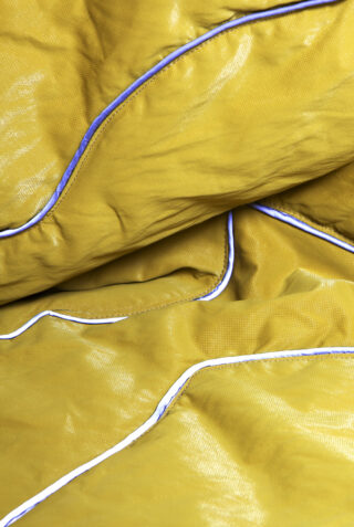 Nahaufnahme eines zerknitterten gelben Stoffes mit glänzender Textur und blau-weißem Besatz an den Rändern.