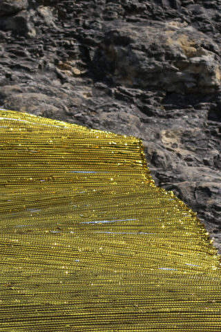 Ein Stück goldmetallisches Netzgewebe, das über eine raue, graue Stein- oder Felsoberfläche drapiert ist.
