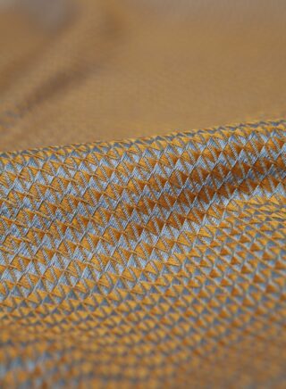 Eine Nahaufnahme eines Stoffes mit einem sich wiederholenden geometrischen Muster in Gelb- und Grautönen, das kleine Rautenformen und eine leichte Textur zeigt.